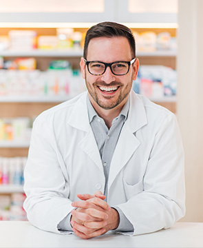 Portrait of a cheerful young pharmacist leaning on a counter at drugstore, looking at camera.